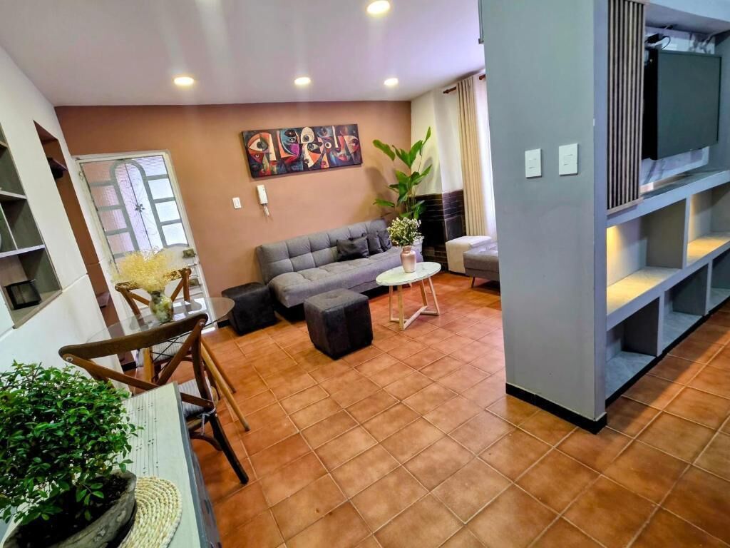 Una sala de estar con un sofá, una mesita redonda, una planta en maceta y un televisor sobre un mueble bajo.