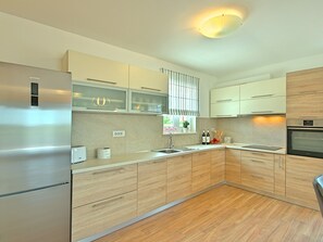 A modern kitchen with a built-in oven, stainless steel refrigerator, and wooden cabinets. - Villa Mušković by Interhome (Tinjan)