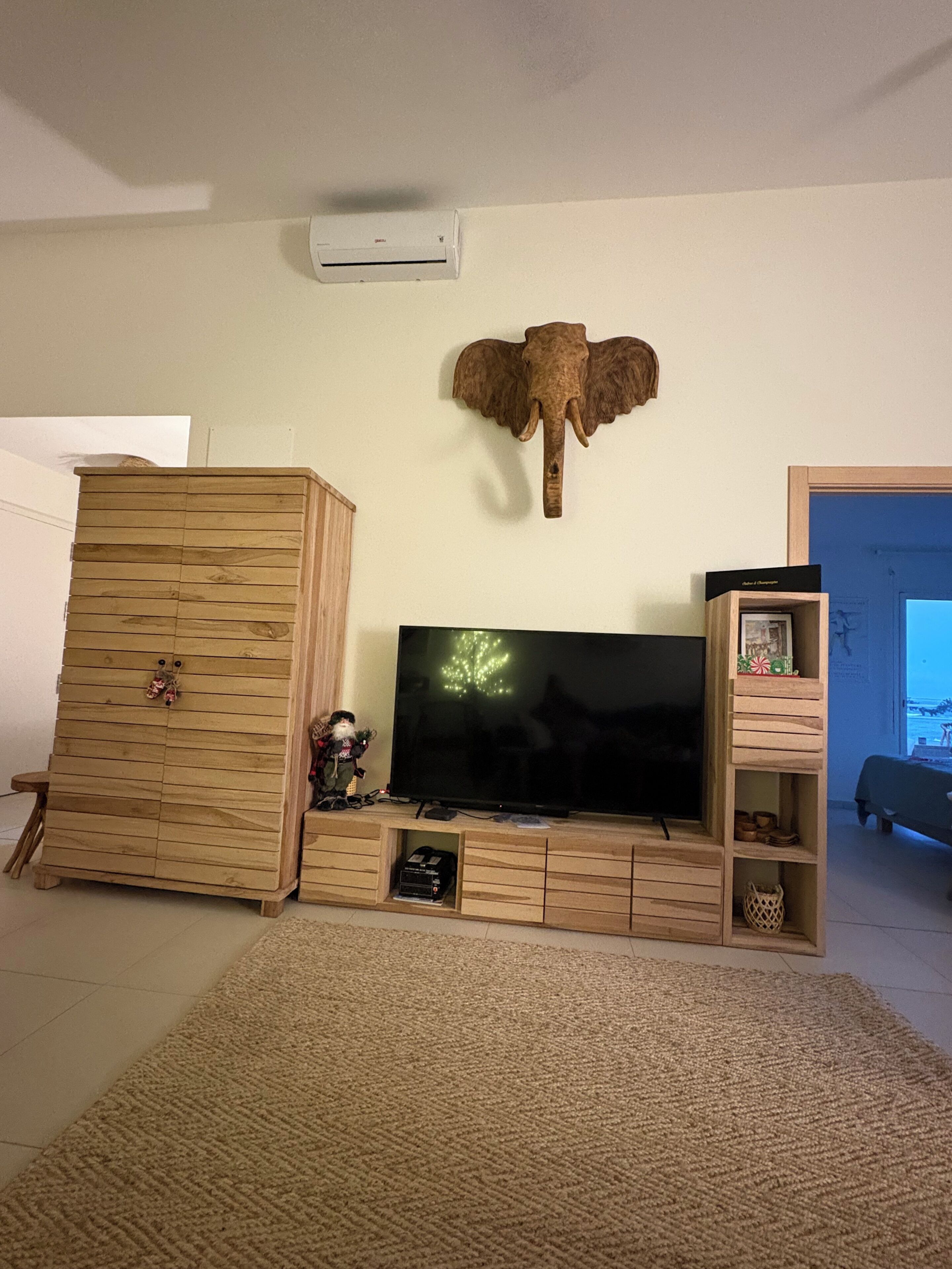 Un saló amb televisió, un moble de fusta, una decoració amb forma de cap d'elefant i una petita estant amb objectes.