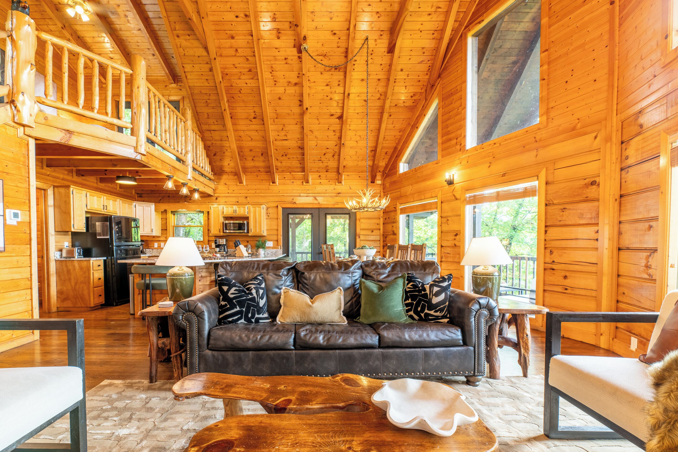 A log cabin interior with a living room, kitchen, and dining area, featuring wooden walls and a high ceiling.