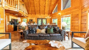 L’intérieur d’une cabane en rondins comprend un salon, une cuisine et un coin repas, avec des murs en bois et un plafond haut.