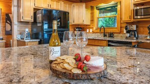 Une cuisine avec des meubles de rangement en bois, un réfrigérateur, un four à micro-ondes et un plan de travail sur lequel se trouvent une bouteille de vin, des verres, des fraises et du fromage.