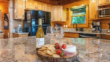A kitchen with wooden cabinets, a refrigerator, a microwave, and a countertop with a bottle of wine, glasses, strawberries, and cheese.