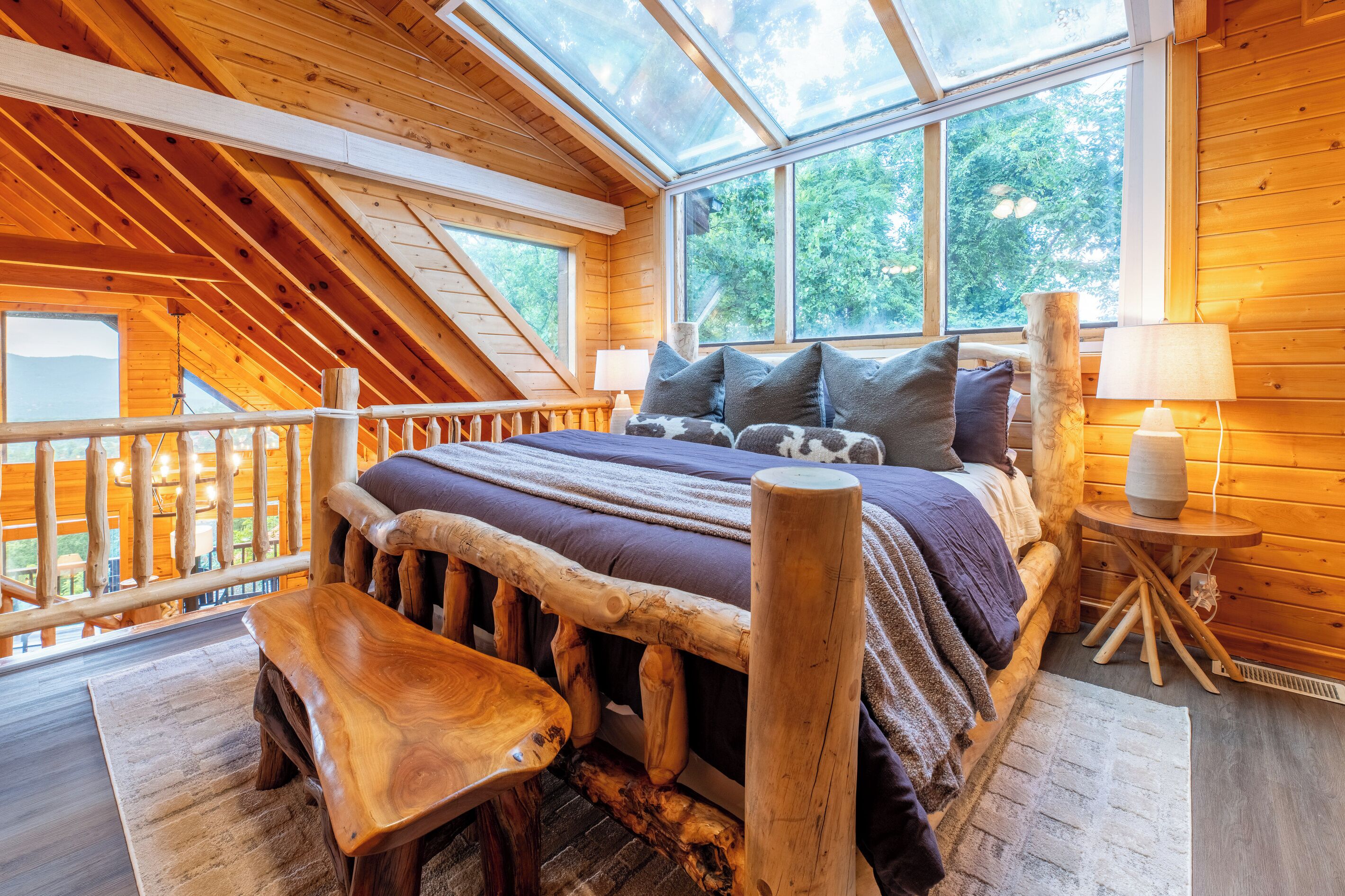 A wooden cabin bedroom with a sloped ceiling, a bed with a wooden headboard, a bench, and a small table.