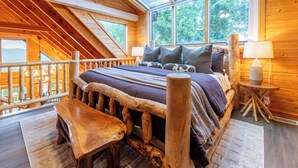 Une chambre dans une cabane en bois, avec un plafond en pente, un lit doté d’une tête de lit en bois, un banc et une petite table.