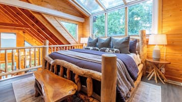 A wooden cabin bedroom with a sloped ceiling, a bed with a wooden headboard, a bench, and a small table.