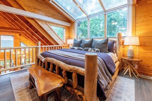 A wooden cabin bedroom with a sloped ceiling, a bed with a wooden headboard, a bench, and a small table. - Long Mountain Views@Skycrest! Sleeps 11, 98" Theater, Hot tub, Firepit, GameRoom (Sevierville)