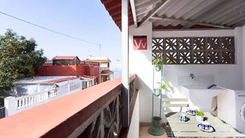 A balcony with a red railing, a white wall with a decorative pattern, a small table with a plant, and a washing machine.