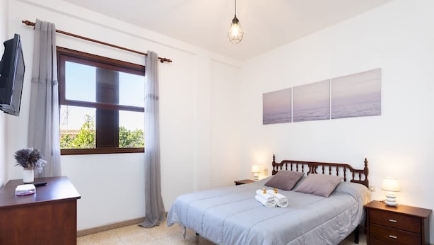 A bedroom with a bed, bedside tables, a desk, a TV, and a window with curtains. - Acogedor Apartamento c Ntrico (Tacoronte)
