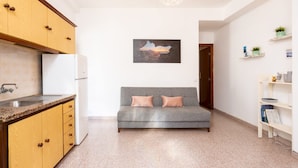 A modern kitchen with wooden cabinets, a white refrigerator, a grey sofa with cushions, a pendant light, and a framed picture on the wall. - Acogedor Apartamento c Ntrico (Tacoronte)