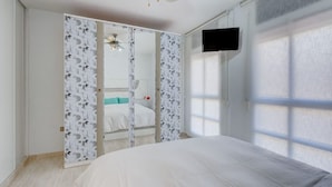 Ein Schlafzimmer mit einem Bett, einem Deckenventilator, einem Fernseher und einem Fenster.