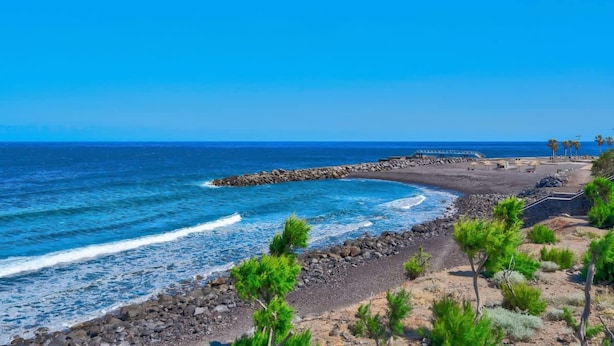 Eine Küstenlandschaft mit felsigem Strand, einer Holzsteganlage und spärlicher Vegetation.