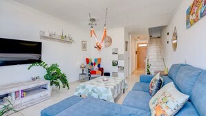 Ein Wohnzimmer mit einem blauen Sofa, einem Couchtisch, einem Fernseher und einer Treppe, die in einen anderen Raum führt.