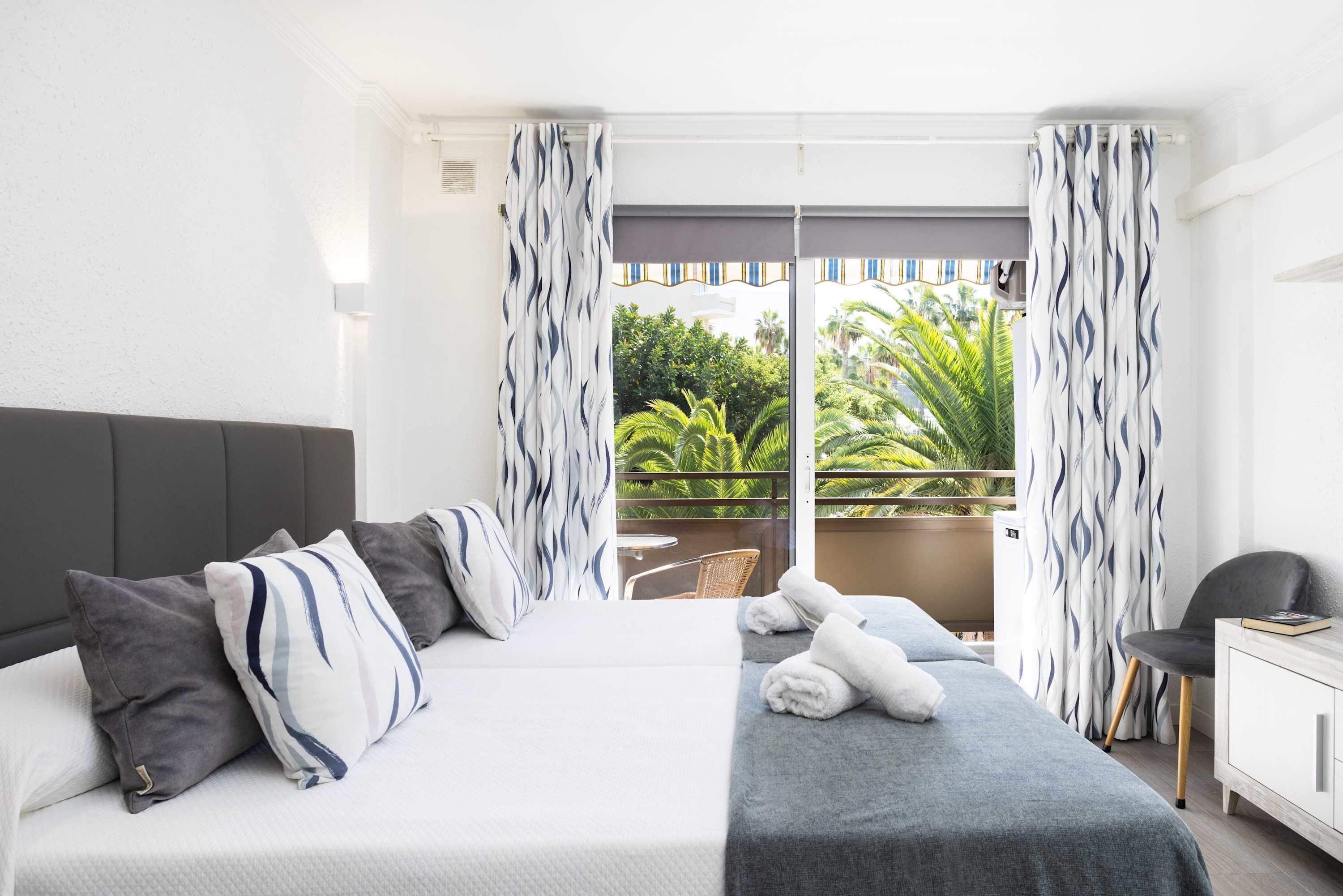 Een hotelkamer met een bed, een tafeltje, een stoel en een balkon met gordijnen.