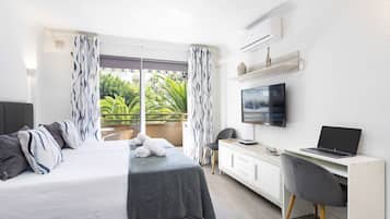 Een moderne hotelkamer met een bed, bureau, televisie en een balkon met uitzicht op groen.