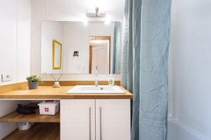 Un baño con un lavamanos blanco, un espejo, un toallero y una cortina de ducha.