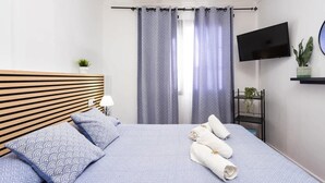A hotel room with a bed, pillows, a TV, a plant, and a curtain. - Apartamento Terraza Los Realejos (Los Realejos)