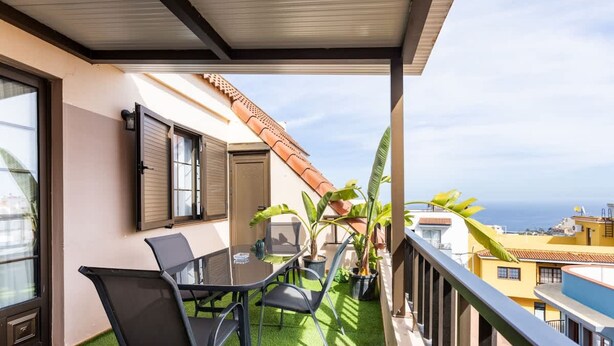A balcony with a table and chairs, a potted plant, and a view of the ocean. - Apartamento Terraza Los Realejos (Los Realejos)