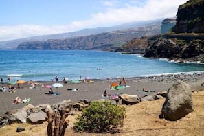 A beach with people, umbrellas, and a rocky coastline. - Apartamento Atardecer Martianez (Puerto de la Cruz)