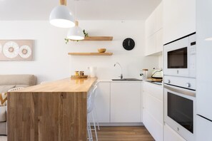 A modern kitchen with white cabinets, a wooden island, a sink, and a microwave. - Apartamento Atardecer Martianez (Puerto de la Cruz)