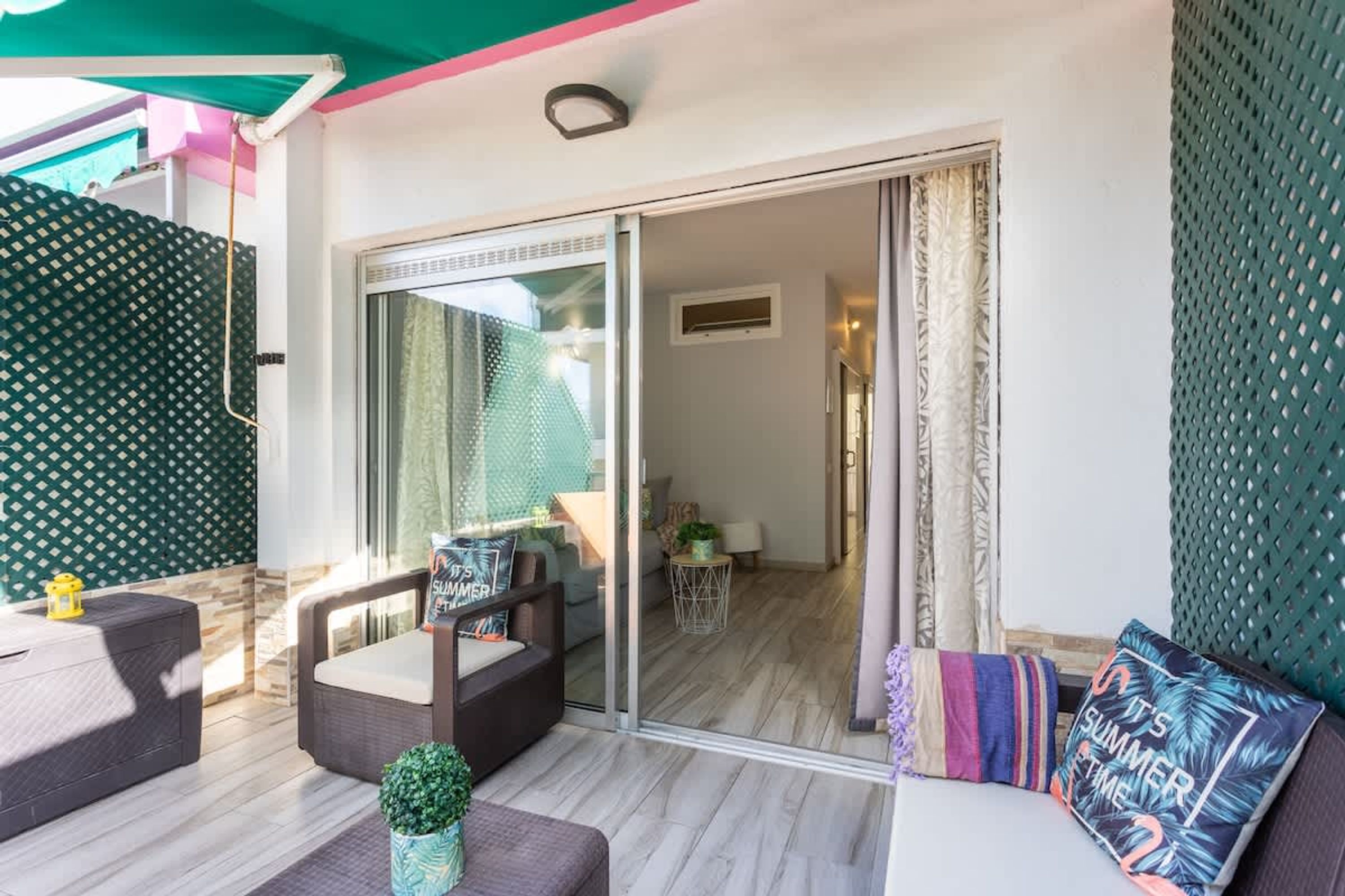 A room with a sliding glass door leading to a balcony, a sofa, a small table, and a potted plant.