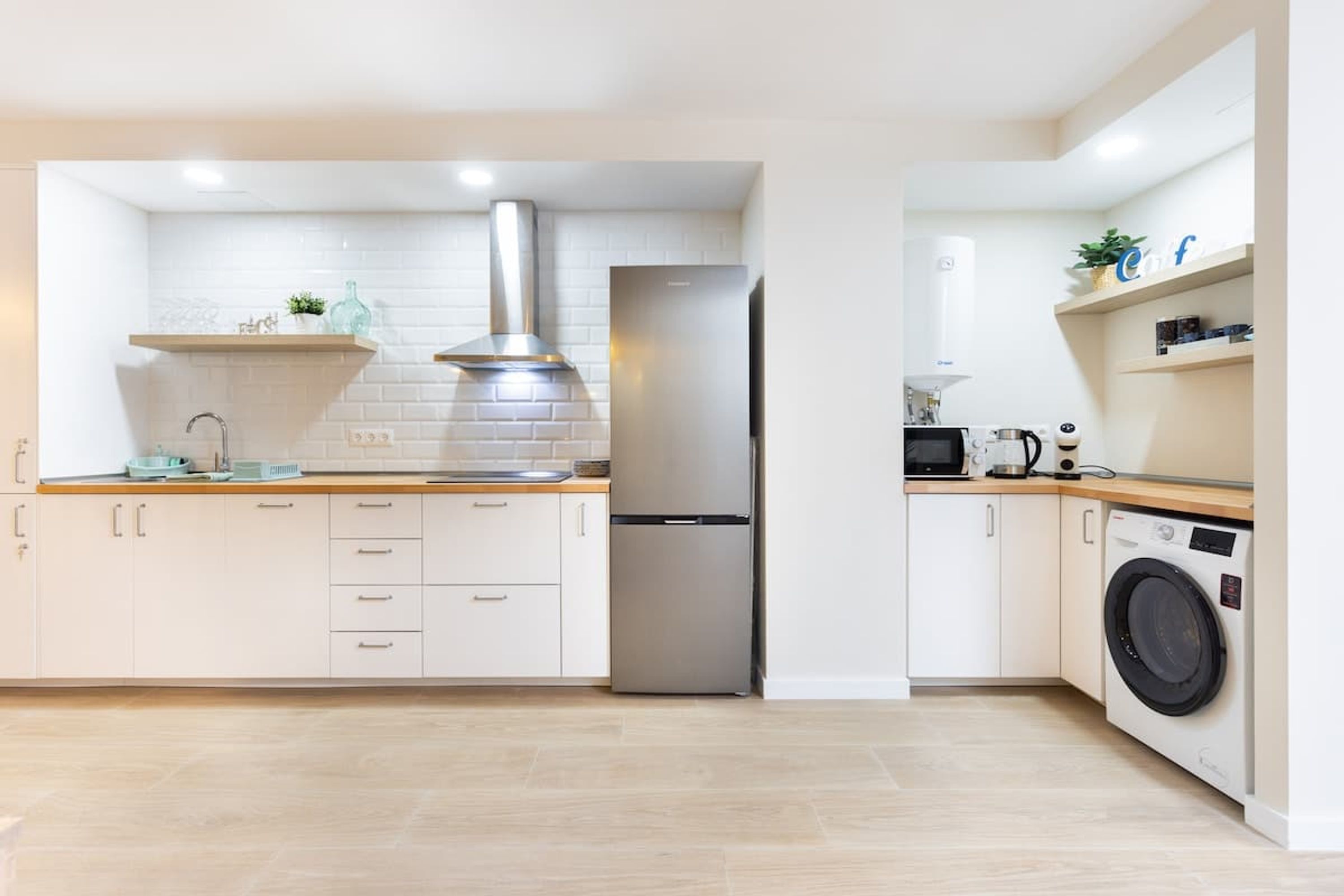 Una cocina moderna con armarios blancos, un refrigerador de acero inoxidable, un horno empotrado y una lavadora.
