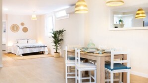 Ein heller Raum mit einem Bett, einem Esstisch mit Stühlen, einem großen Spiegel und Pendelleuchten.