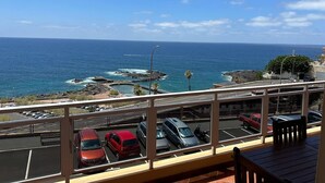 Un balcón con vista al océano y coches estacionados.