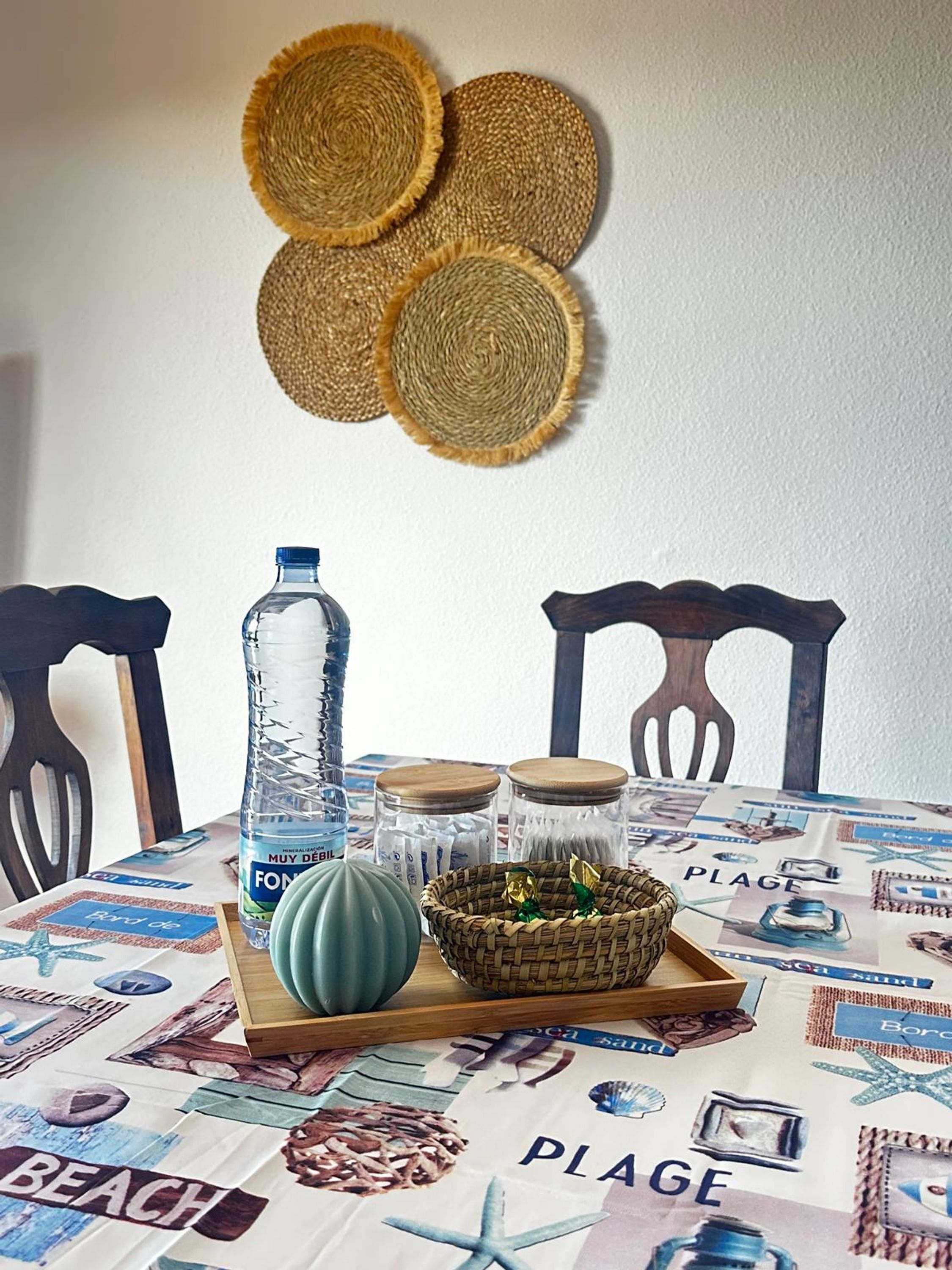 A dining table with a beach-themed tablecloth, a water bottle, a green bowl, and a woven basket with decorative items.