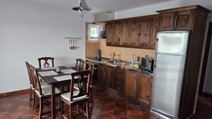Una cocina con armarios de madera, un refrigerador de acero inoxidable, una mesa de comedor con sillas y una lámpara colgante.