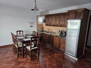 Una cocina con armarios de madera, un refrigerador de acero inoxidable, una mesa de comedor con sillas y una lámpara colgante.