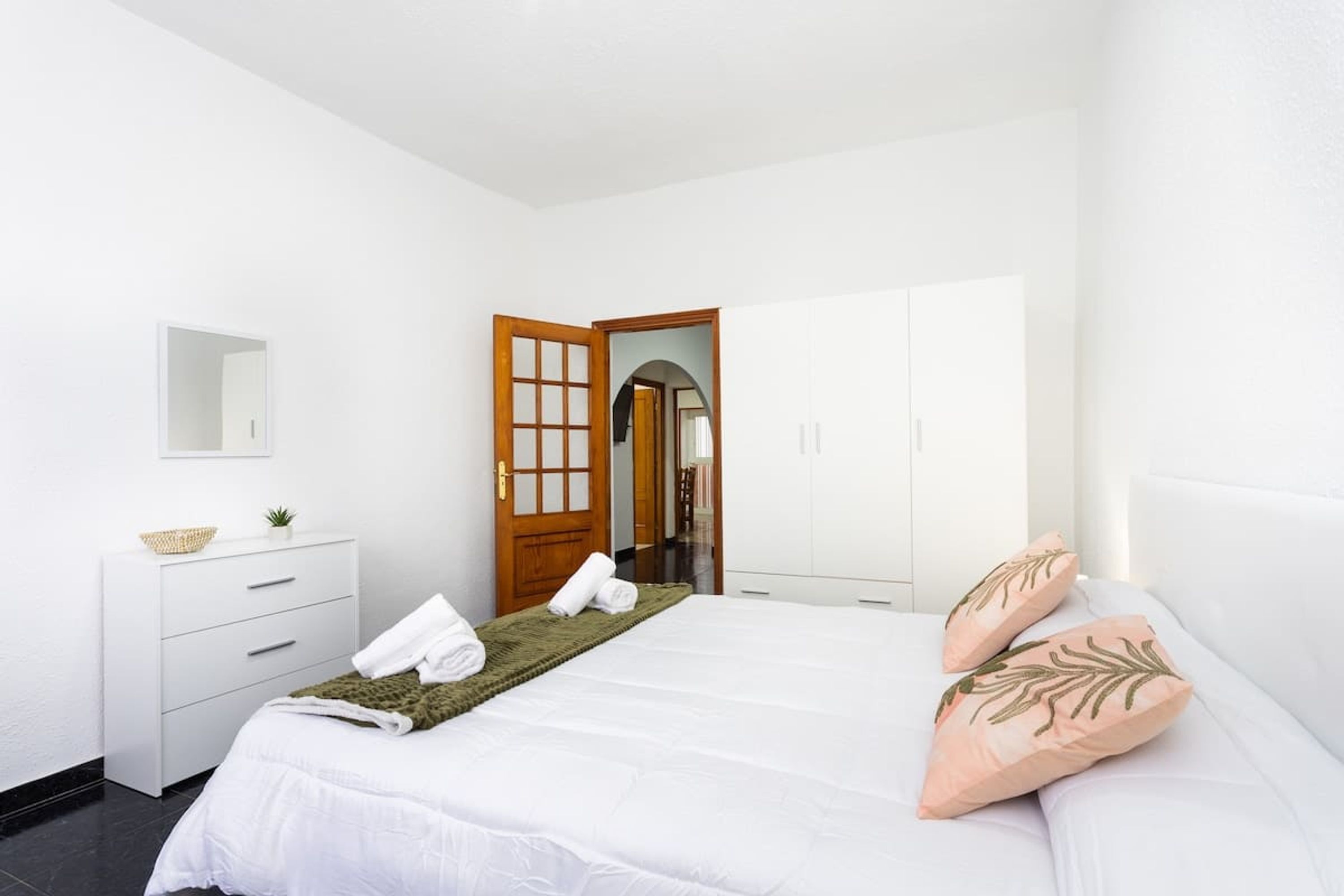 Ein Schlafzimmer mit einem Bett, einem Schminktisch, einem Spiegel und einer Tür zu einem anderen Raum.