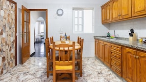 Een keuken met een marmeren vloer, houten keukenkastjes, een eettafel met stoelen en een uitzicht door een open deur naar een andere kamer.