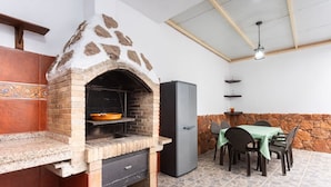 Een buitenkeuken met een bakoven, een koelkast en een eettafel met stoelen.