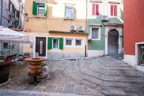 A narrow cobblestone street with buildings on either side, featuring traditional shutters and a small outdoor seating area with a table and chairs. - Nobile Studio in the Historic Town (Koper)