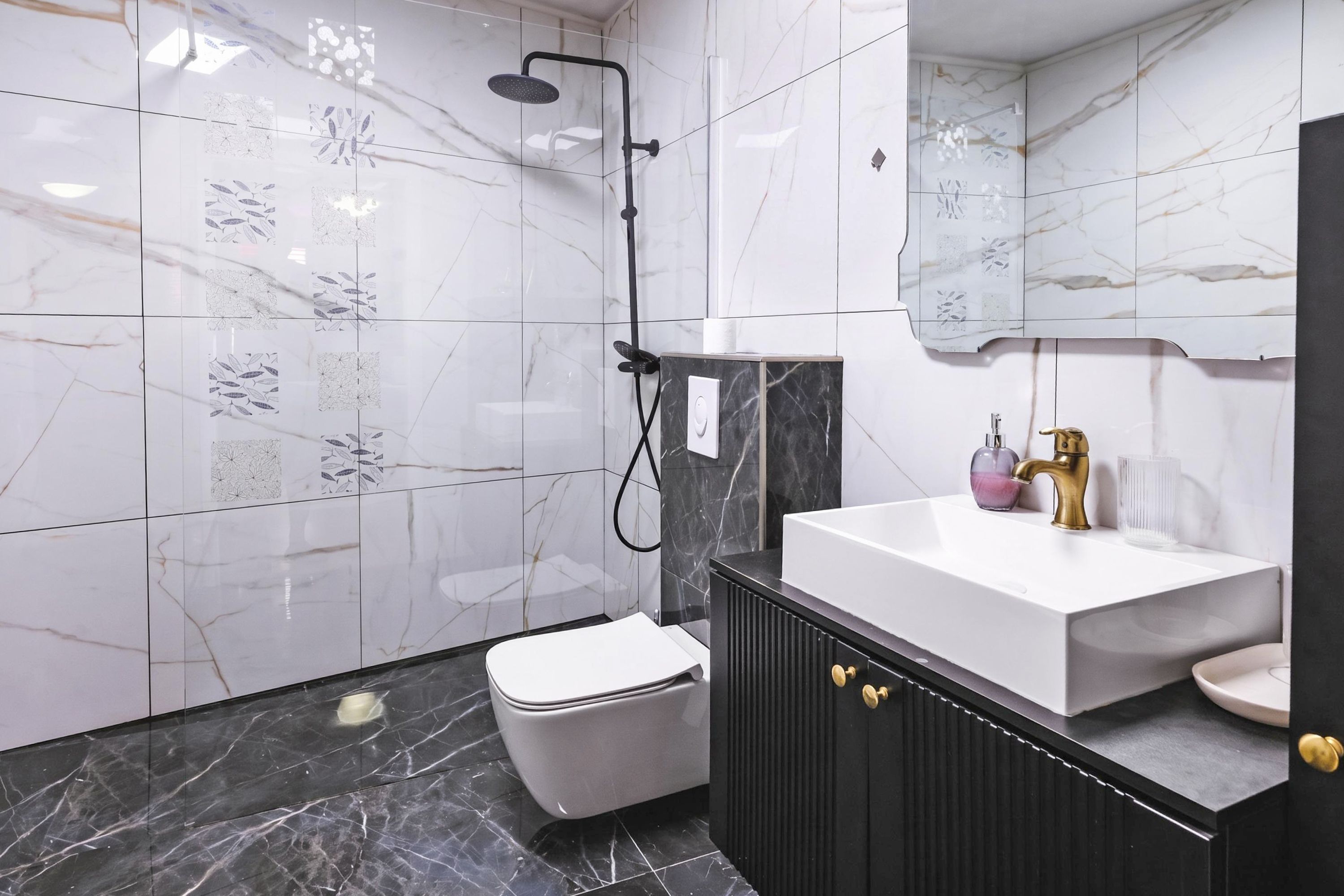 Un bagno con un WC bianco, un mobile lavabo nero con maniglie dorate, un lavandino bianco e una doccia con un tubo nero.