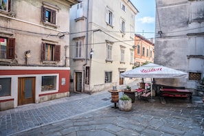 A narrow street with cobblestone pavement, traditional European buildings with shuttered windows, and a café with an umbrella. - Nobile Studio in the Historic Town (Koper)