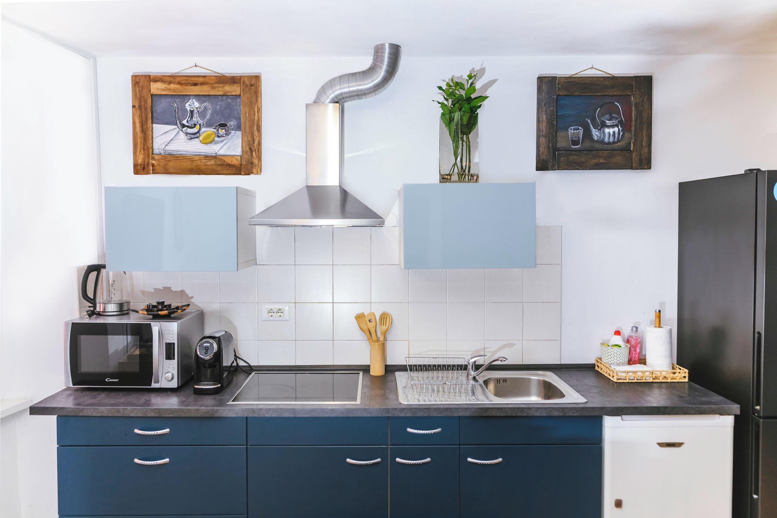A kitchen with a microwave, toaster, sink, cabinet, and a stainless steel range hood.