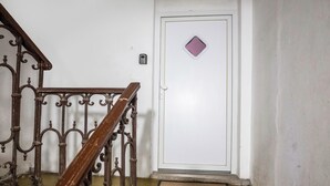 Una escala amb barana de metall decorativa que condueix a una porta blanca amb un petit finestral de forma de diamant.
