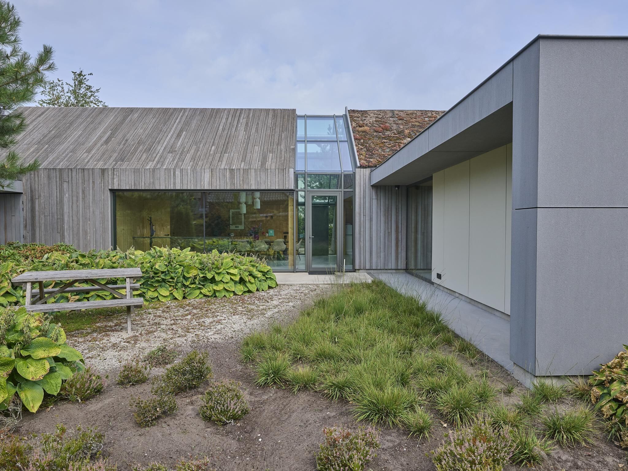 A modern building with a wooden facade, a glass entrance, and a gravel pathway leading to a bench.
