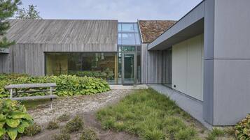 A modern building with a wooden facade, a glass entrance, and a gravel pathway leading to a bench.