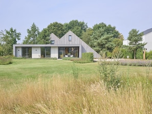 Ein modernes Haus mit einer großen Glasfront, einem Essbereich und einem gepflegten Rasen.
