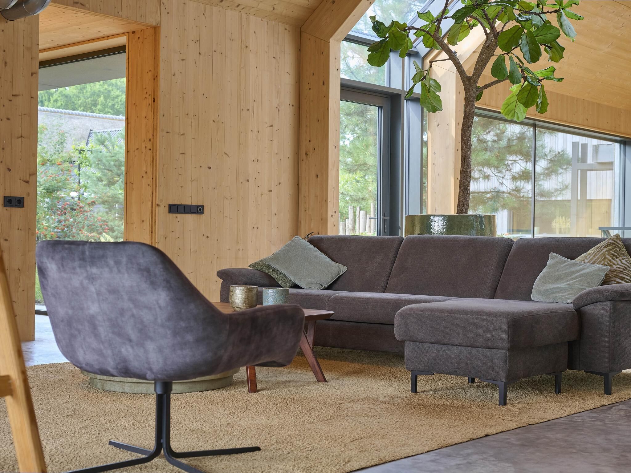 Una sala de estar moderna con un sofá gris, un sillón a juego y un ventanal con vista a árboles.