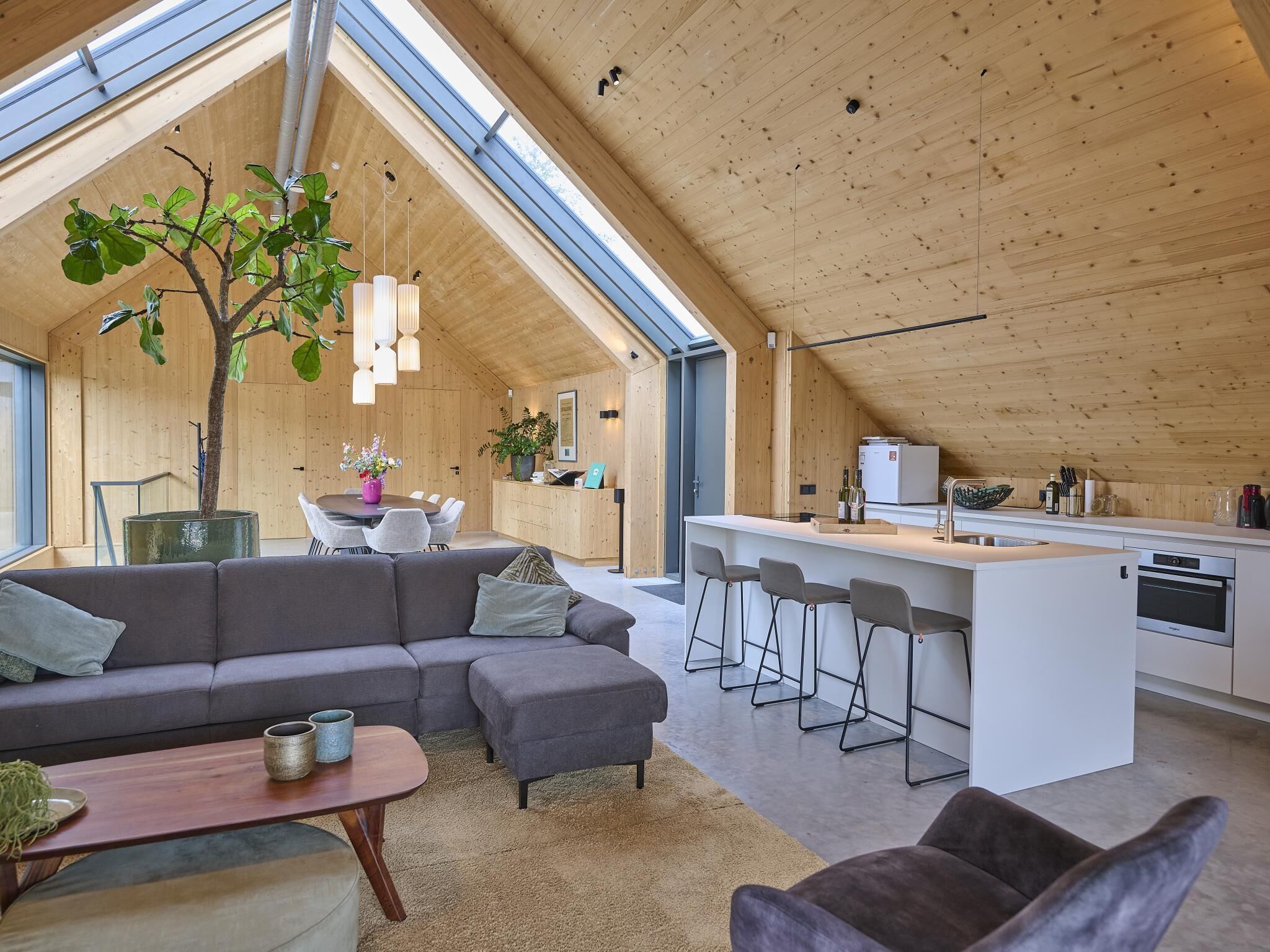A modern interior with a dining area, a sofa, a kitchen, and a large tree.