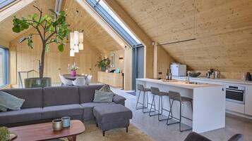 A modern interior with a dining area, a sofa, a kitchen, and a large tree.