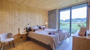 A bedroom with a large bed, a chair, a bedside table, and a view of the outdoors.
