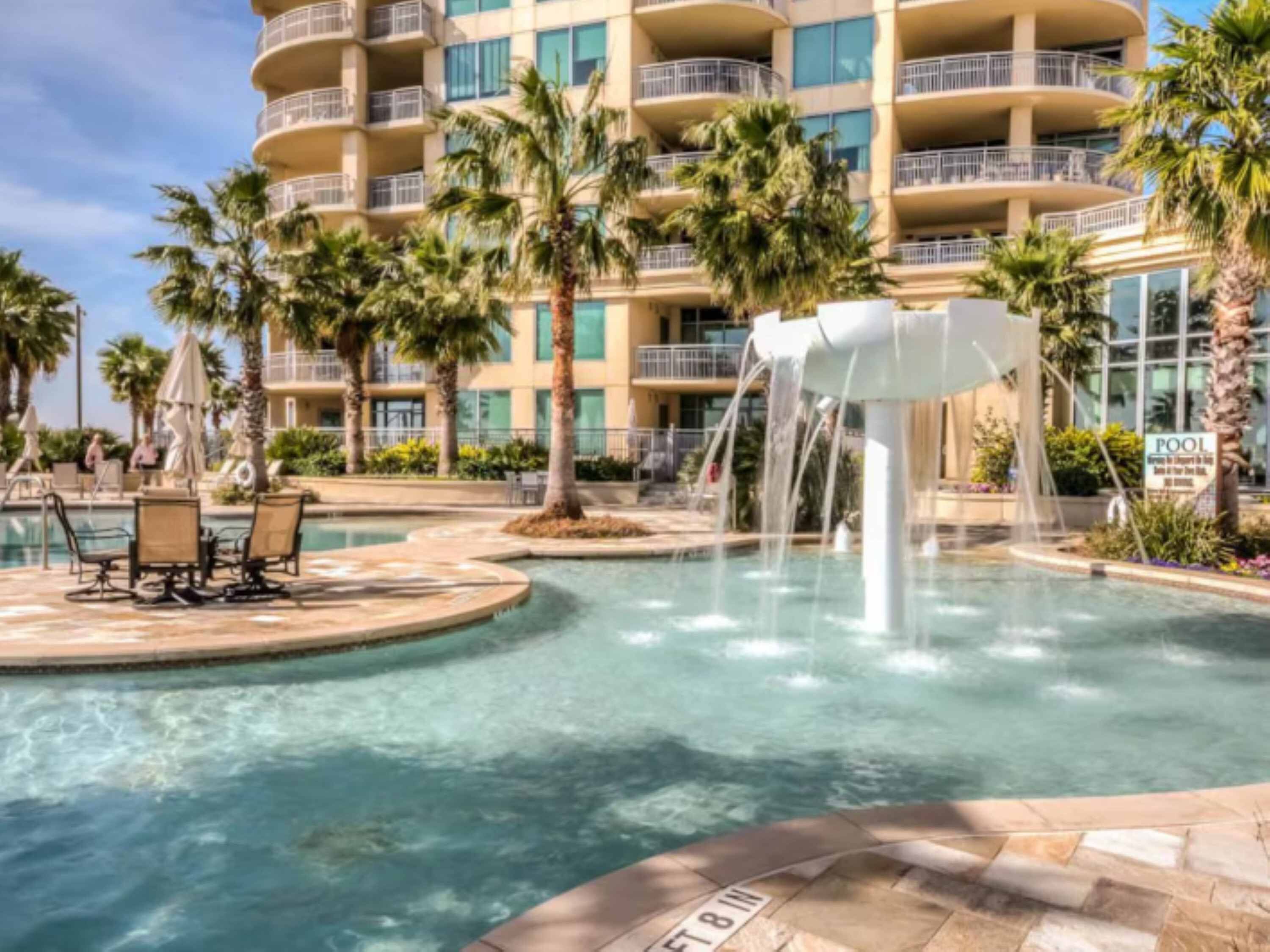 A hotel pool with a water feature, palm trees, and lounge chairs.