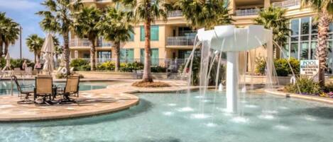 A hotel pool with a water feature, palm trees, and lounge chairs.
