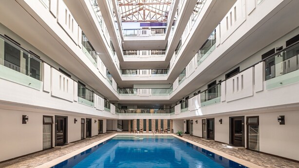 A large indoor swimming pool with a central open area, surrounded by multiple floors with balconies and glass railings.