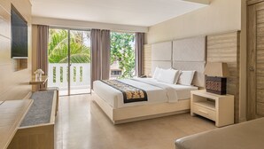 A modern hotel room with a large bed, a bedside table, a TV, and a balcony with a view of greenery.